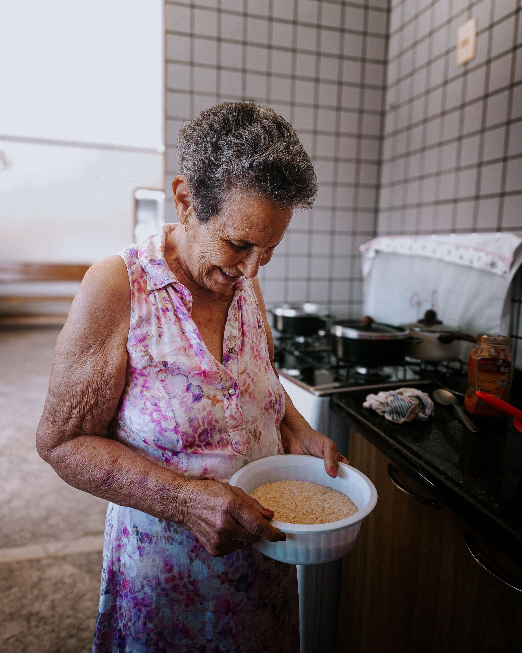 Senhora idosa segurando uma tigela de arroz na cozinha de casa, concentrada no preparo